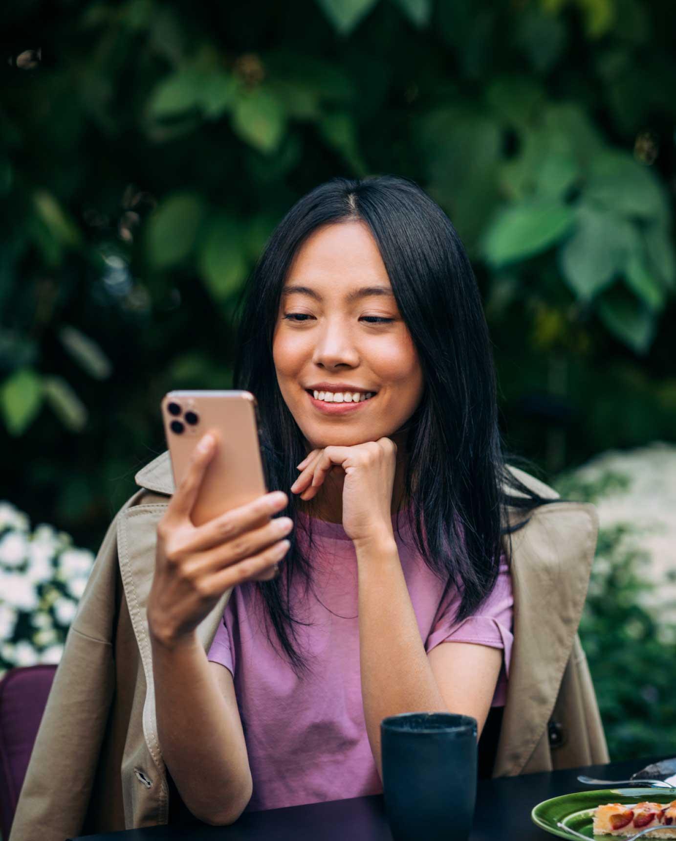 woman sitting at garden patio table smiling and looking at smart phone